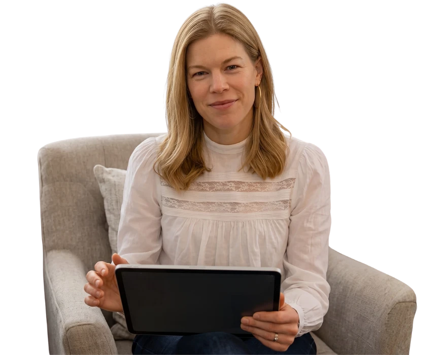 Smiling woman holding a tablet for a Mental Wellness Montclair Virtual Therapy session while sitting in an armchair.